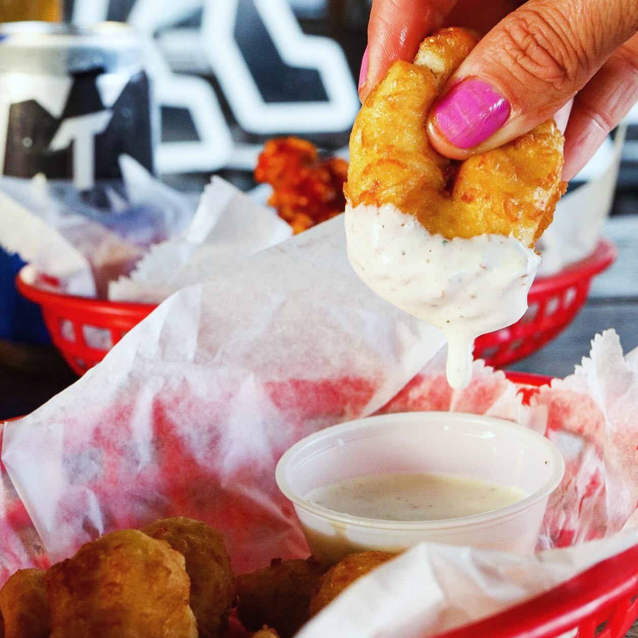 A hand dips a fried onion ring into a white sauce, dripping.