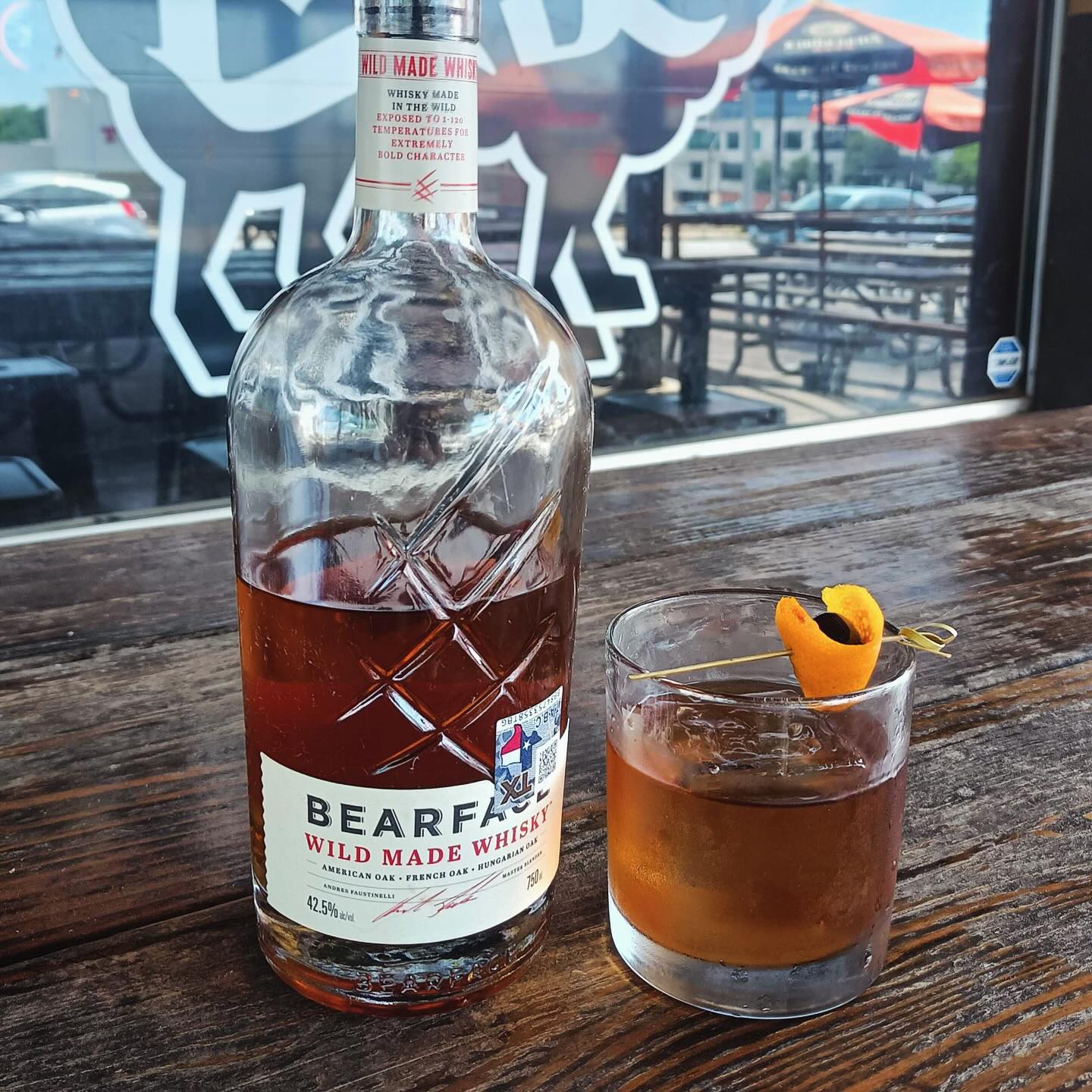 Bottle of Bearface Wild Made Whisky next to a garnished cocktail.