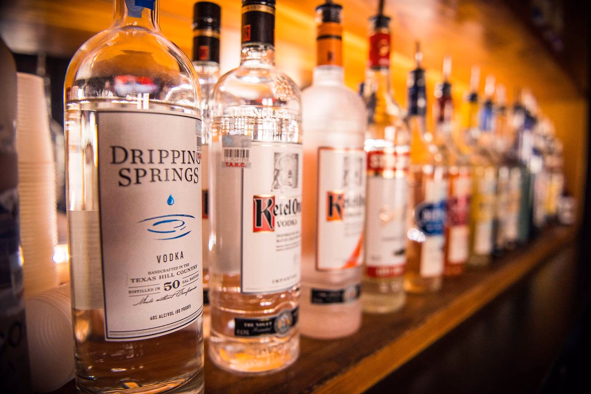 Row of vodka and liquor bottles on a wooden bar shelf.
