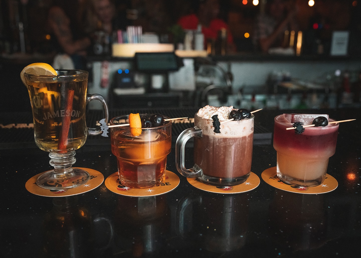 Four assorted drinks with Halloween-themed garnishes on a bar.