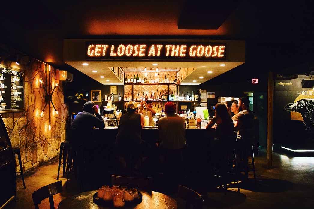 A bartender mixes drinks for customers seated at a dimly lit bar.