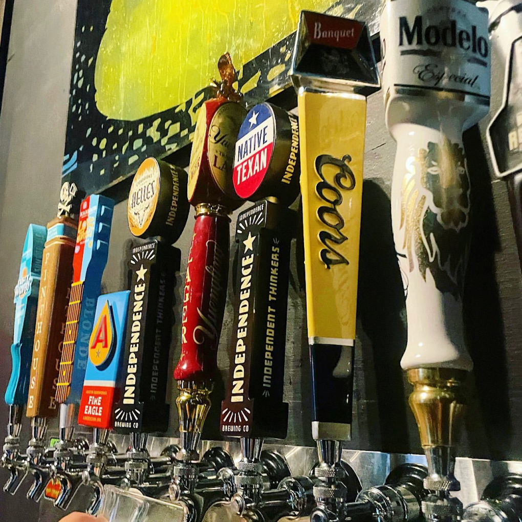 Variety of beer tap handles at a bar, one pouring.