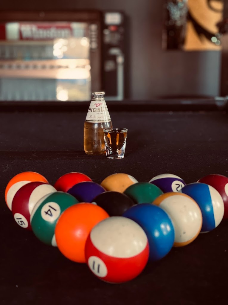 Racked pool balls, beer bottle, and shot glass on a pool table.