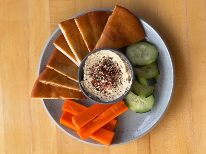 Hummus with pita bread, cucumber slices, and carrot sticks on a plate.