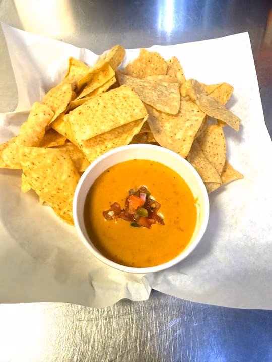 Tortilla chips and a cup of queso topped with pico de gallo.