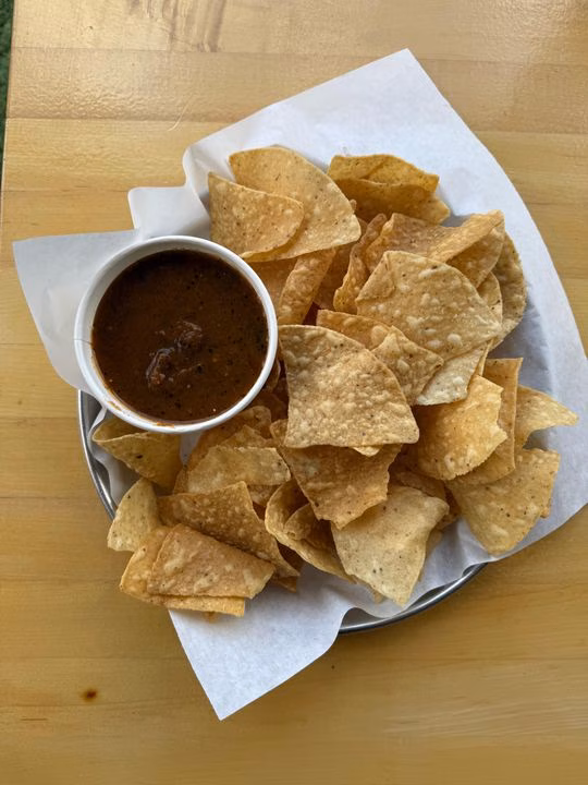 A plate of tortilla chips with a cup of dark chunky dip.