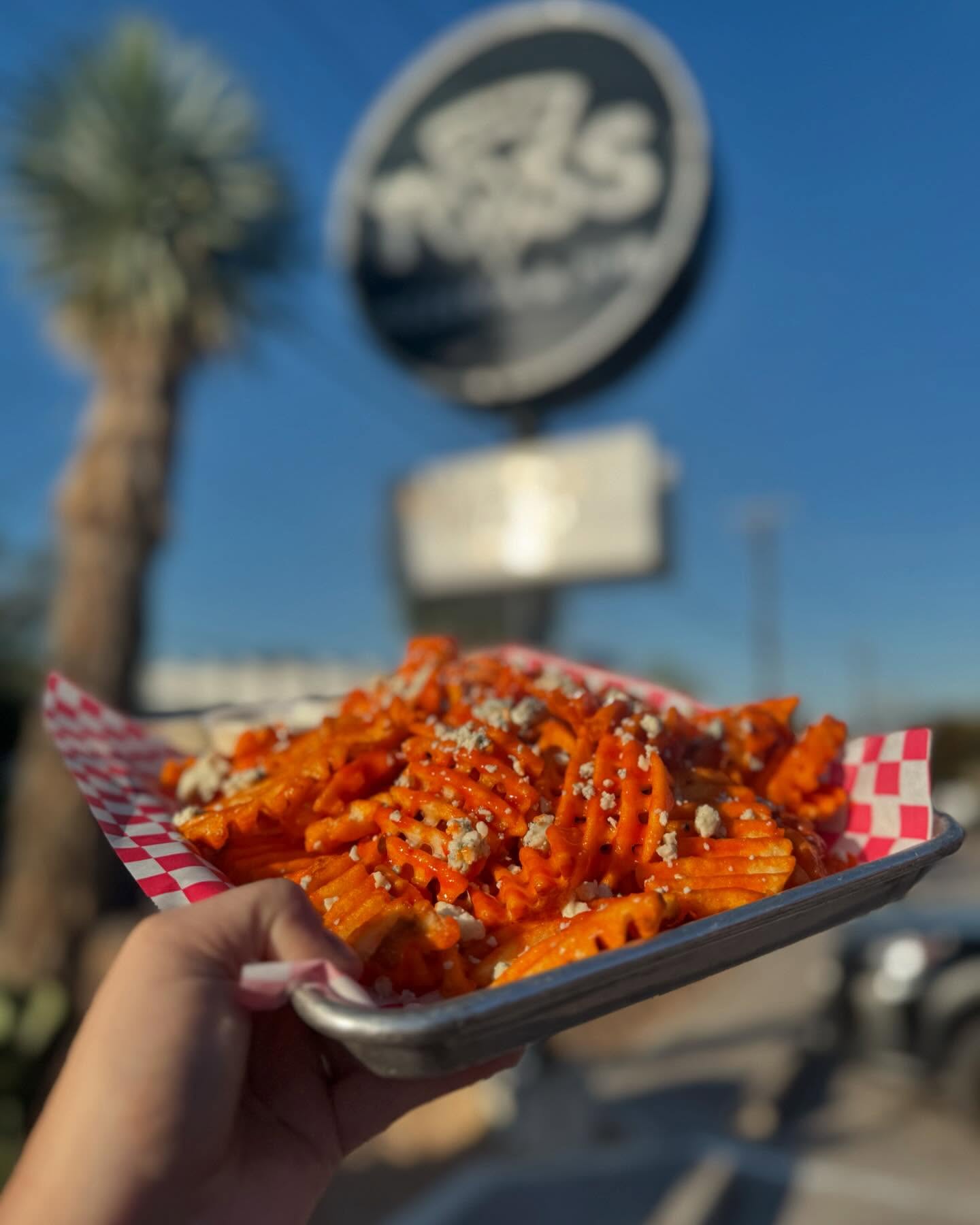 Hand holding a tray of waffle fries with orange sauce and blue cheese.