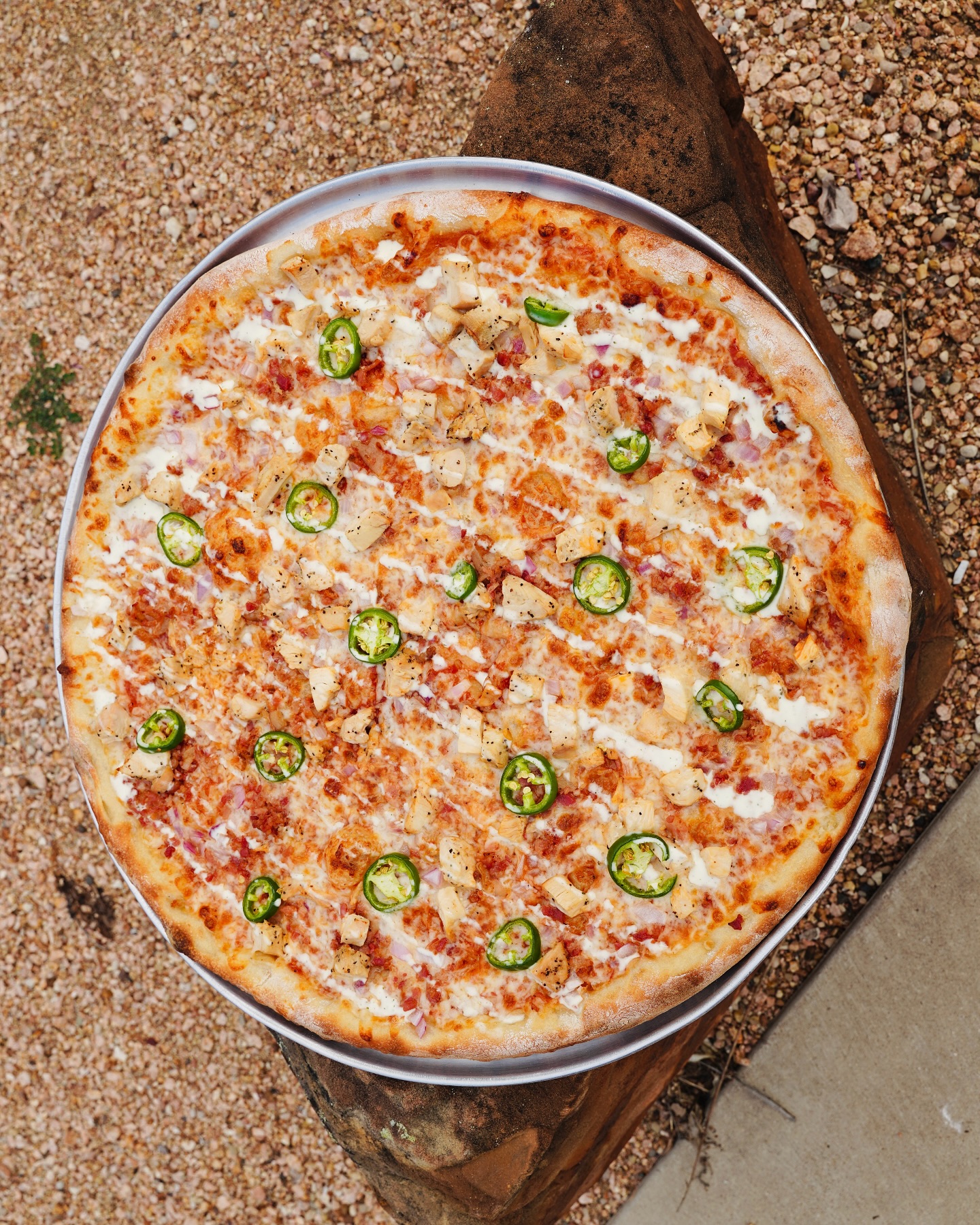 Whole chicken, jalapeño, and red onion pizza with white sauce drizzle.
