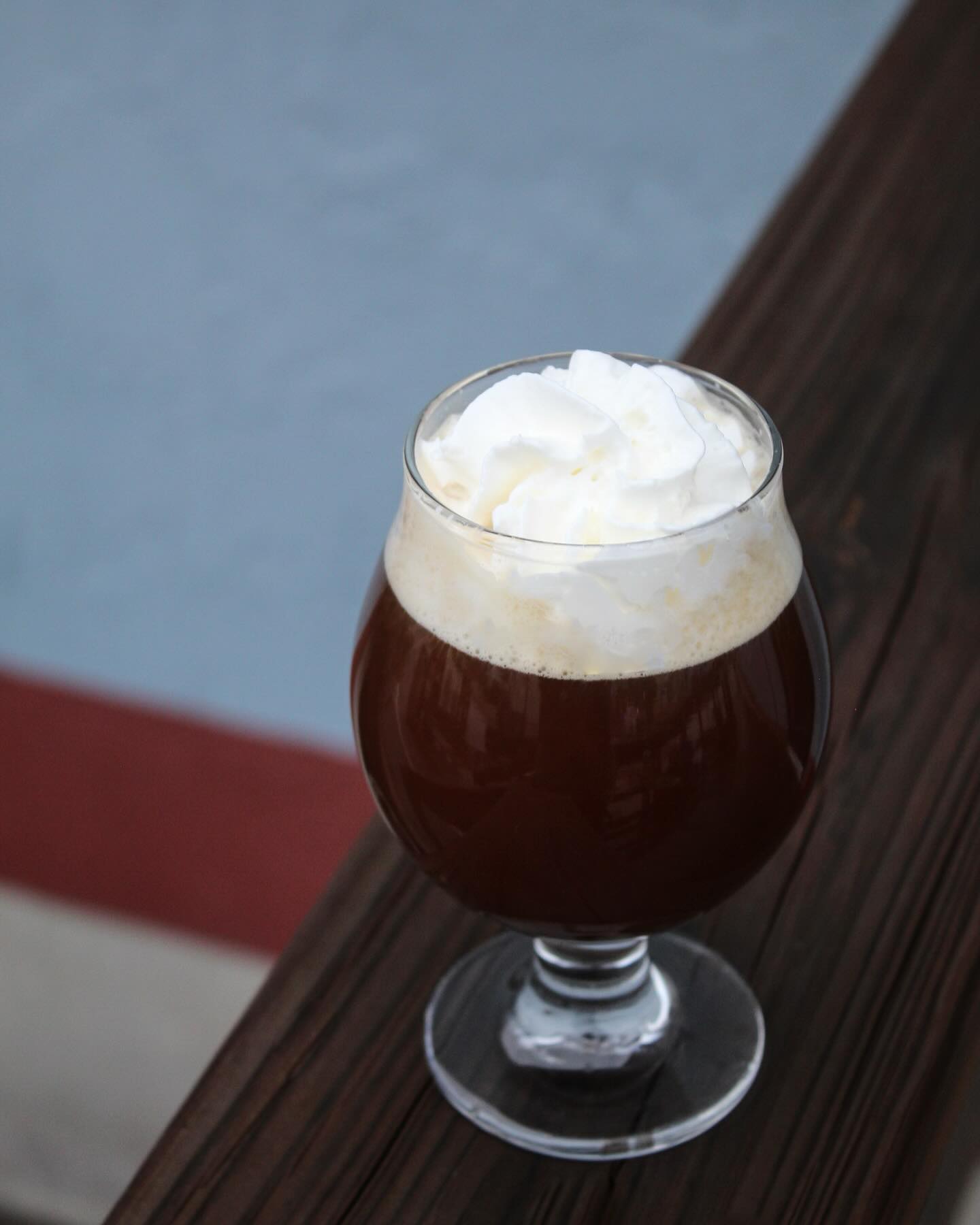 Dark beverage with whipped cream in a stemmed glass on wood.