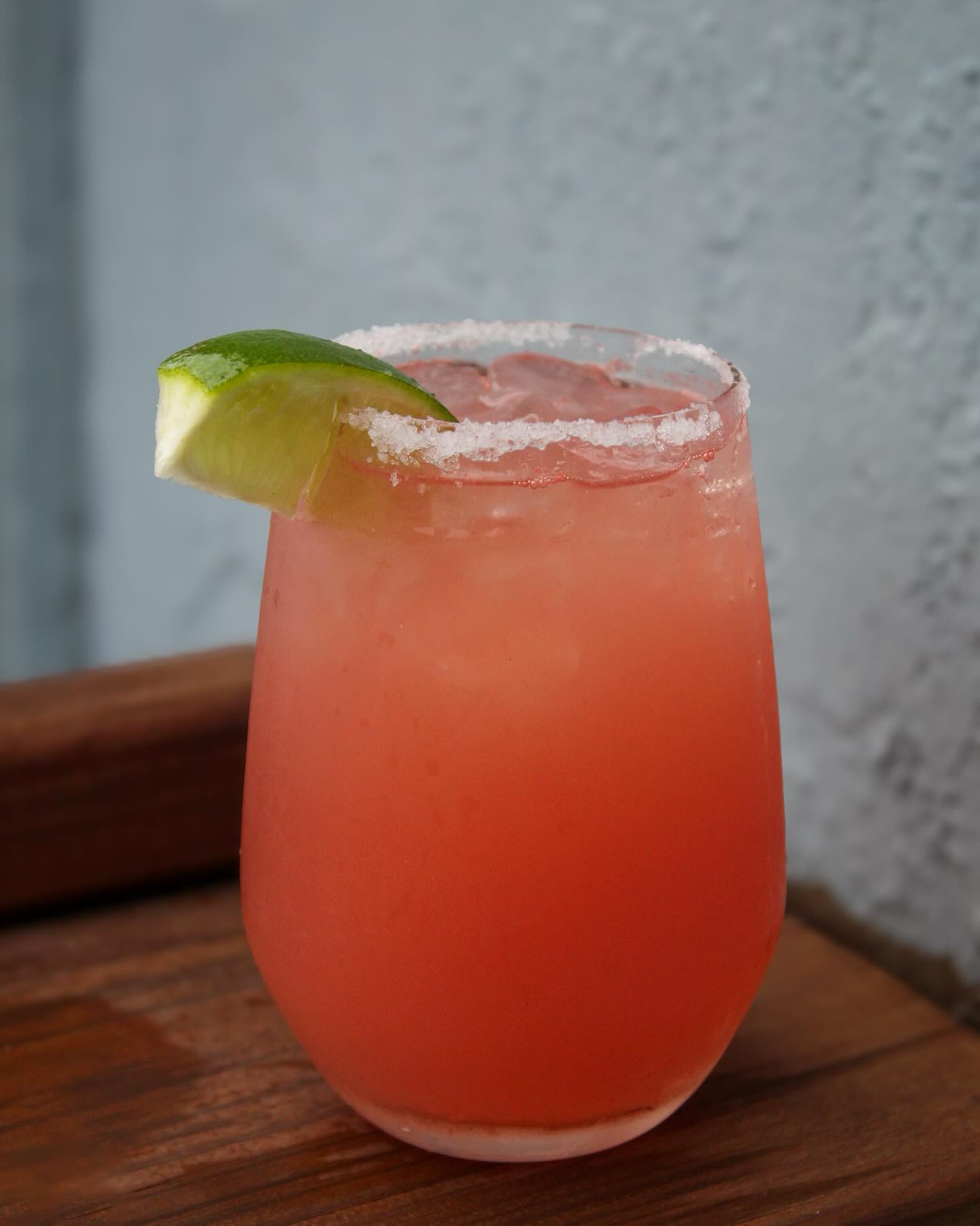 Pink drink in glass with salt rim and lime wedge.