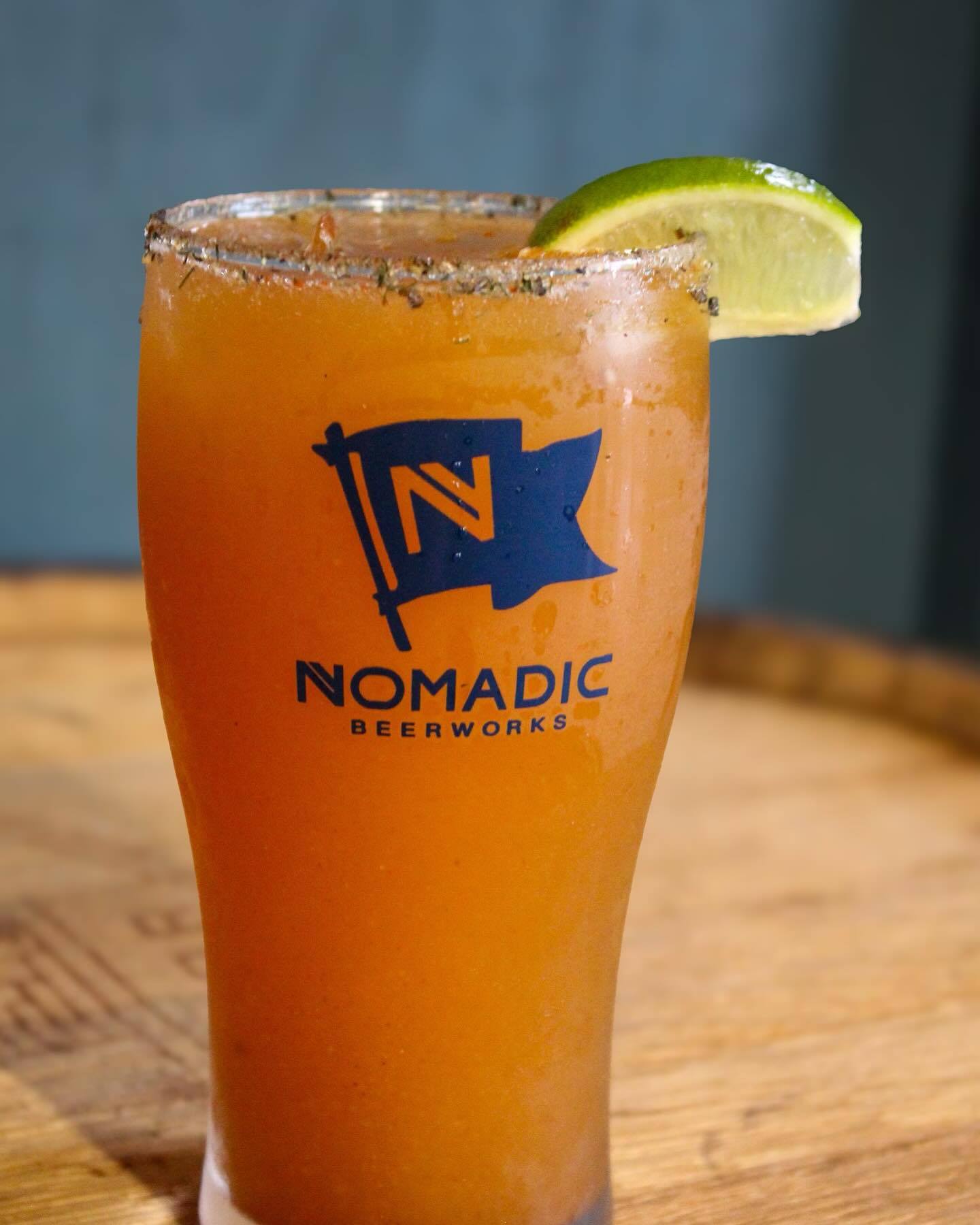 Orange drink in a Nomadic Beerworks glass with lime and seasoned rim.