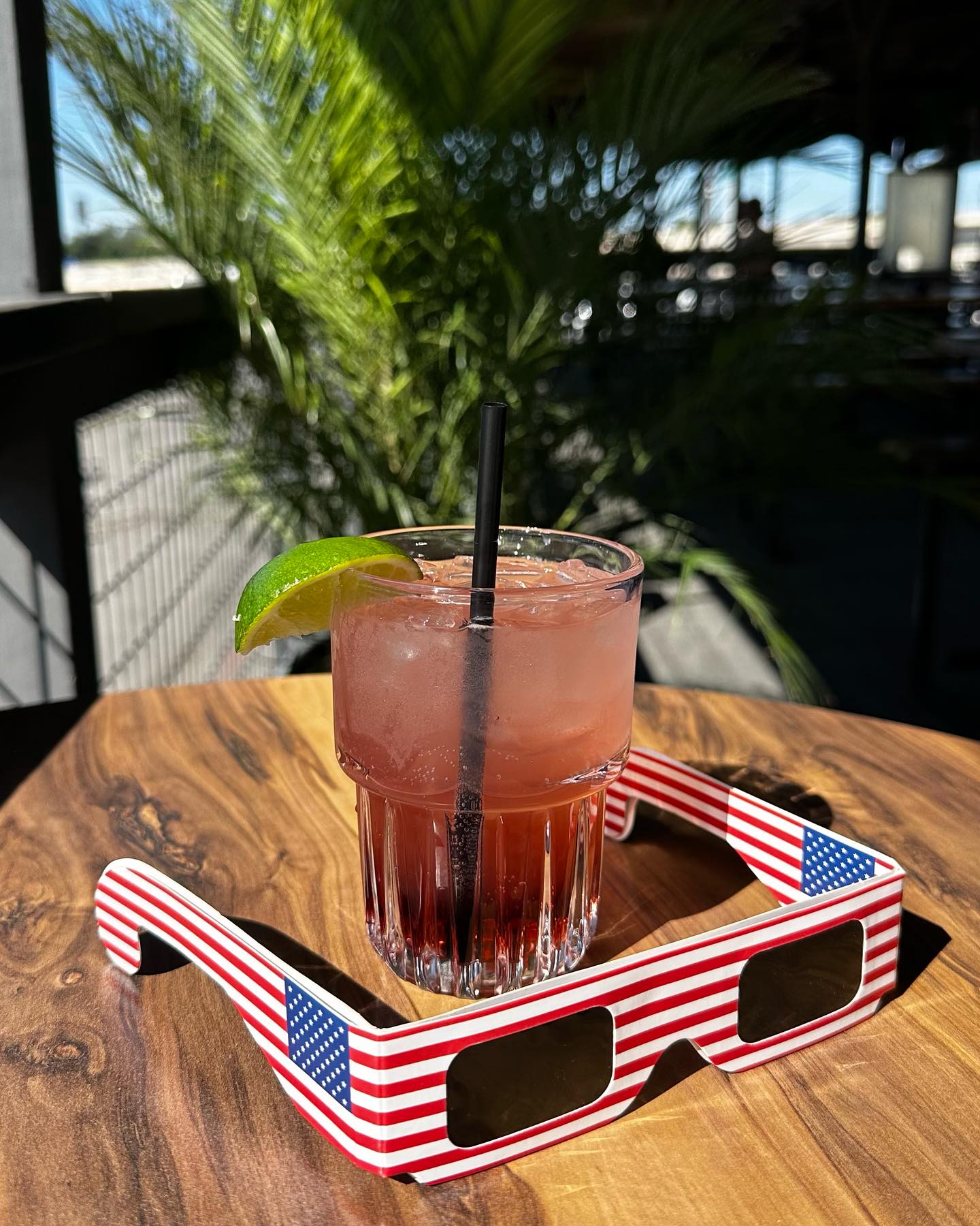 Pink cocktail with lime, black straw, and American flag glasses.