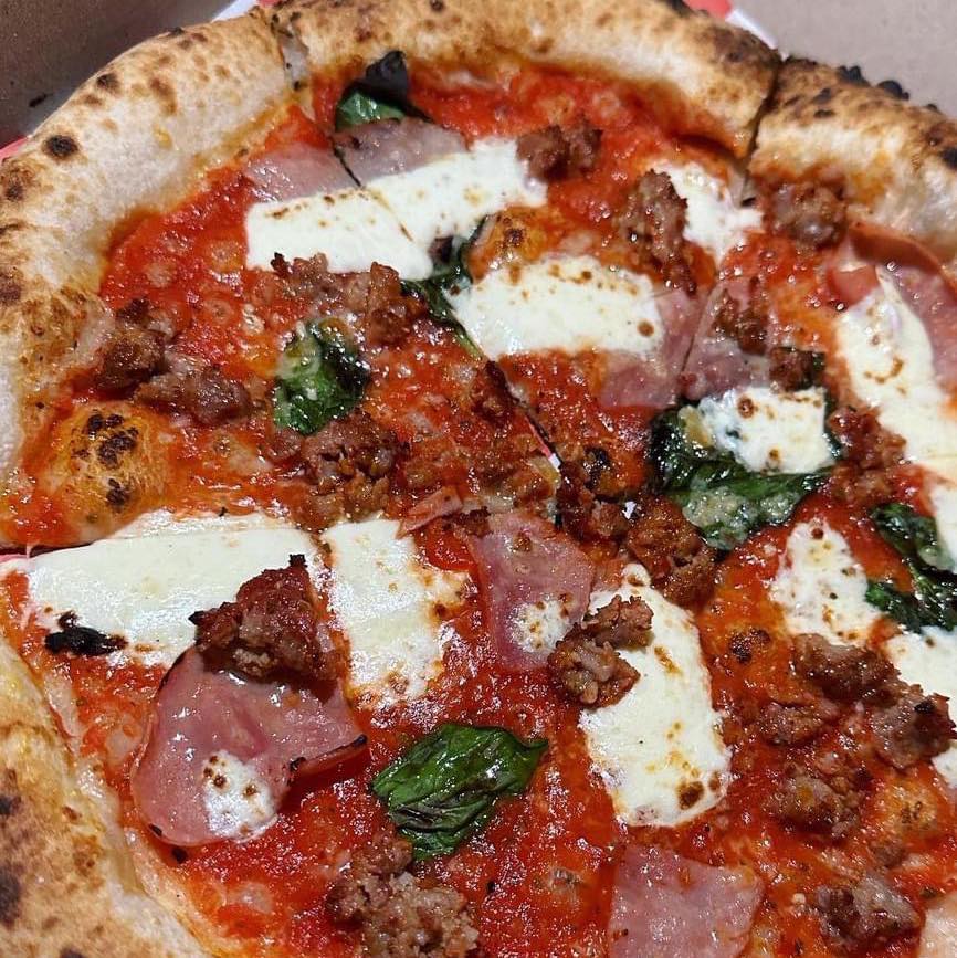 Whole pizza with sausage, ham, mozzarella, basil, and tomato sauce.