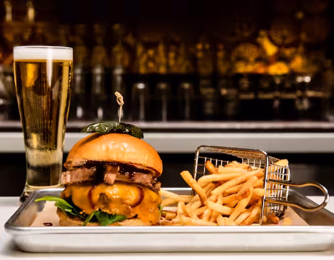 A cheeseburger, basket of fries, and a tall glass of beer.