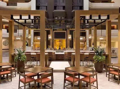 Indoor hotel bar and lounge with tables, chairs, and illuminated counter.