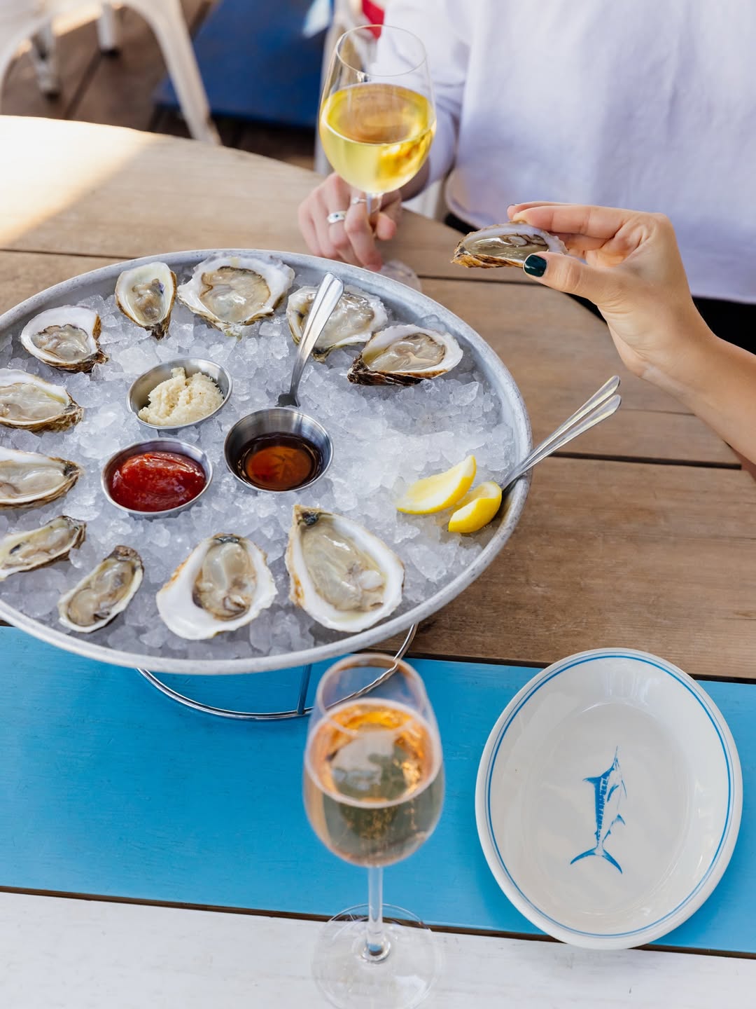 Fresh oysters on ice, sauces, lemon, and wine glasses on a table.