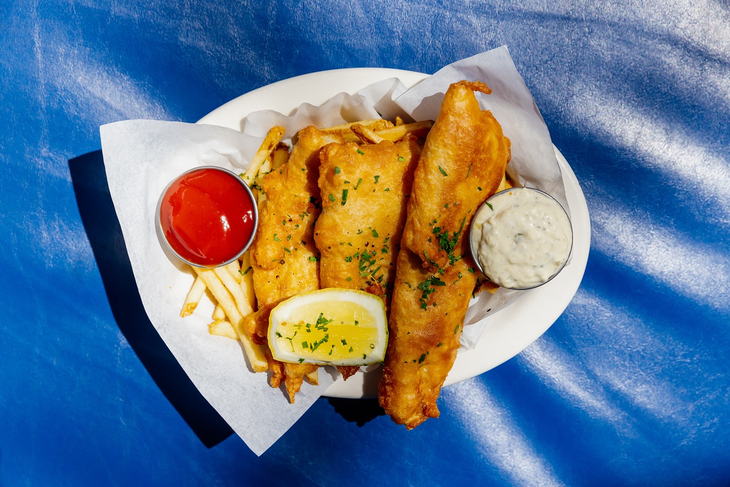 Fish and chips with ketchup, tartar sauce, and a lemon wedge.