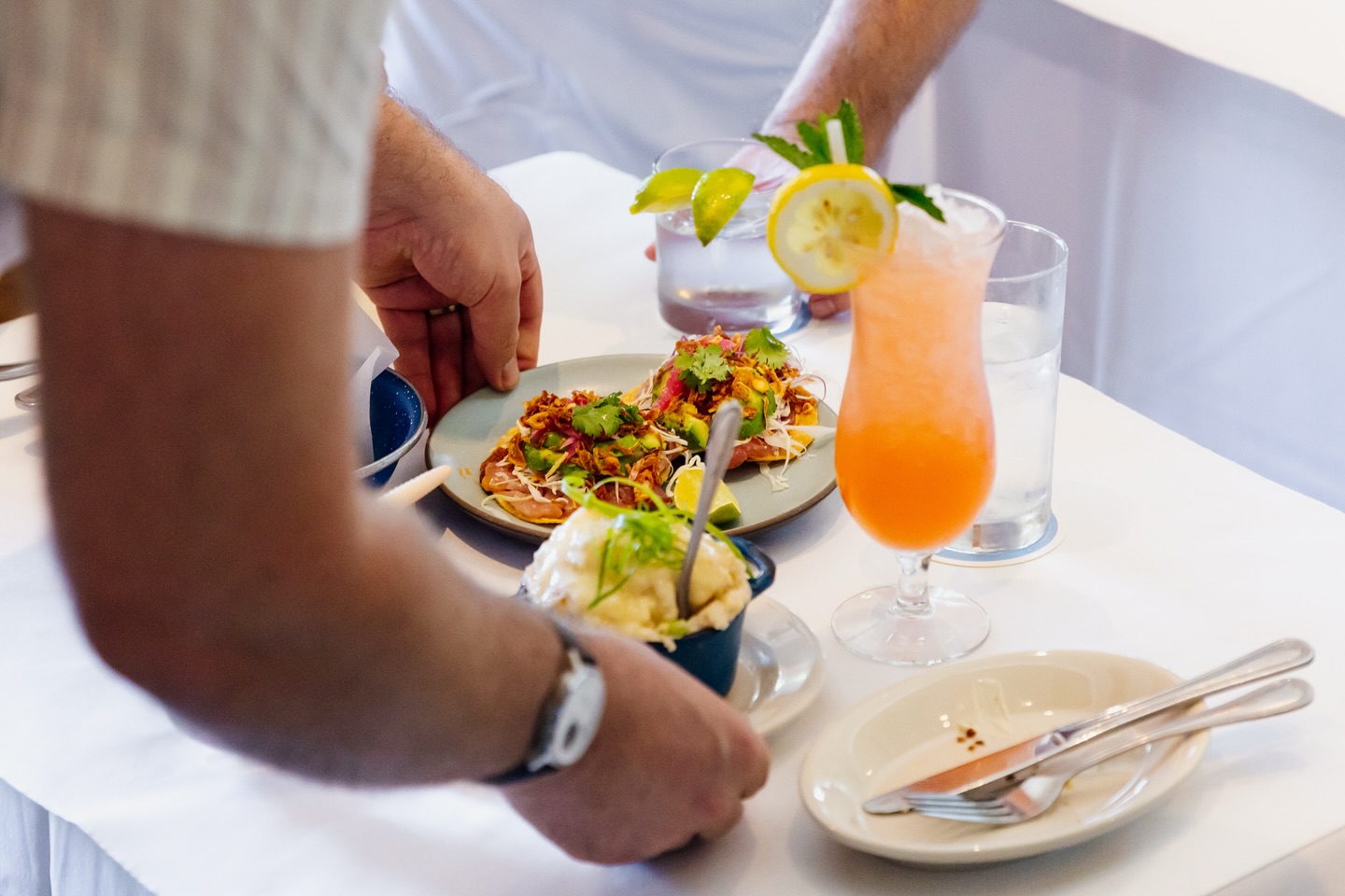Two sets of hands serving various dishes and drinks on a table.