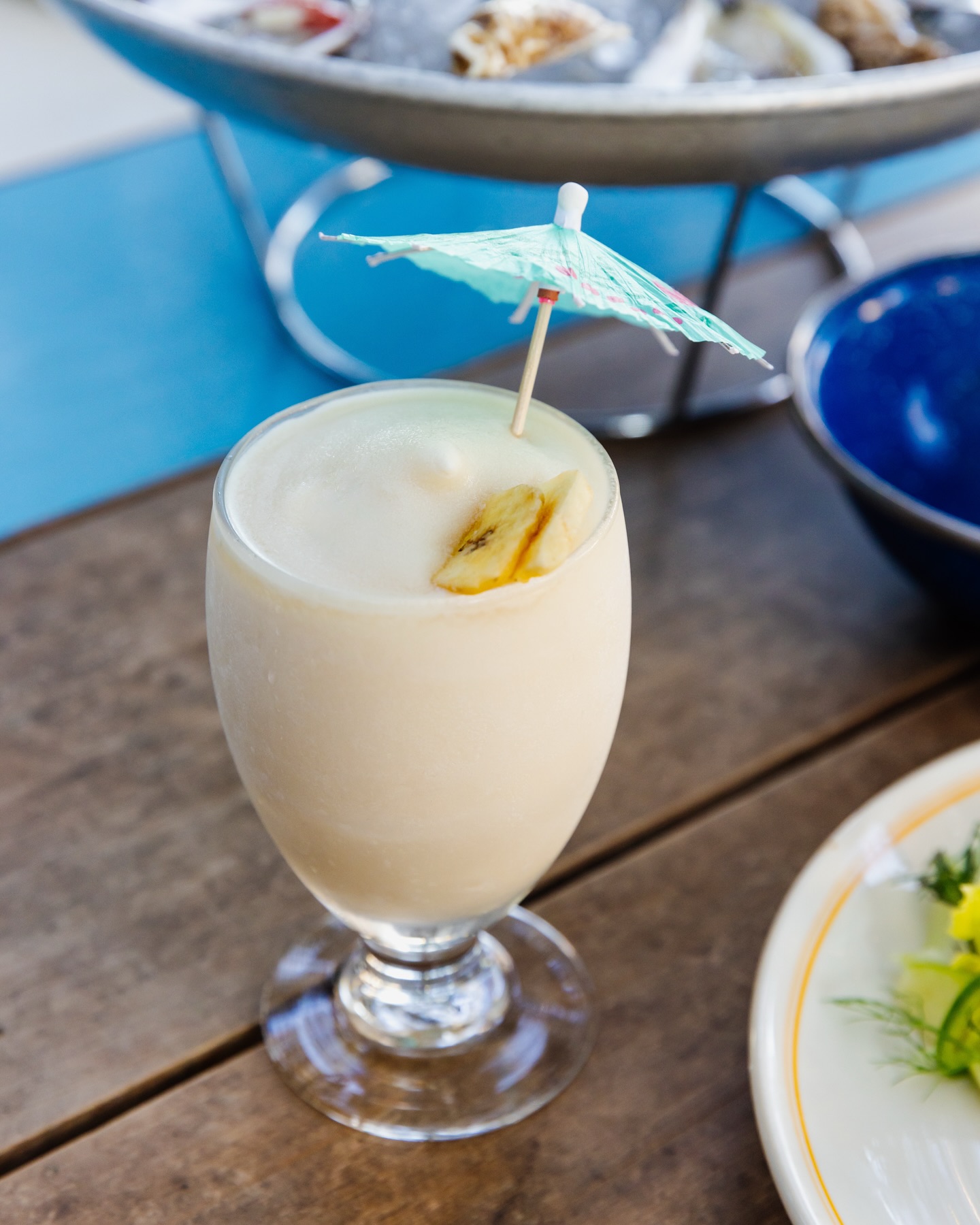 Frozen white drink with banana slices and a blue paper umbrella.