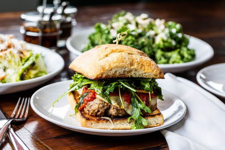 Meatball sandwich on ciabatta bread with arugula, cheese, and sauce.