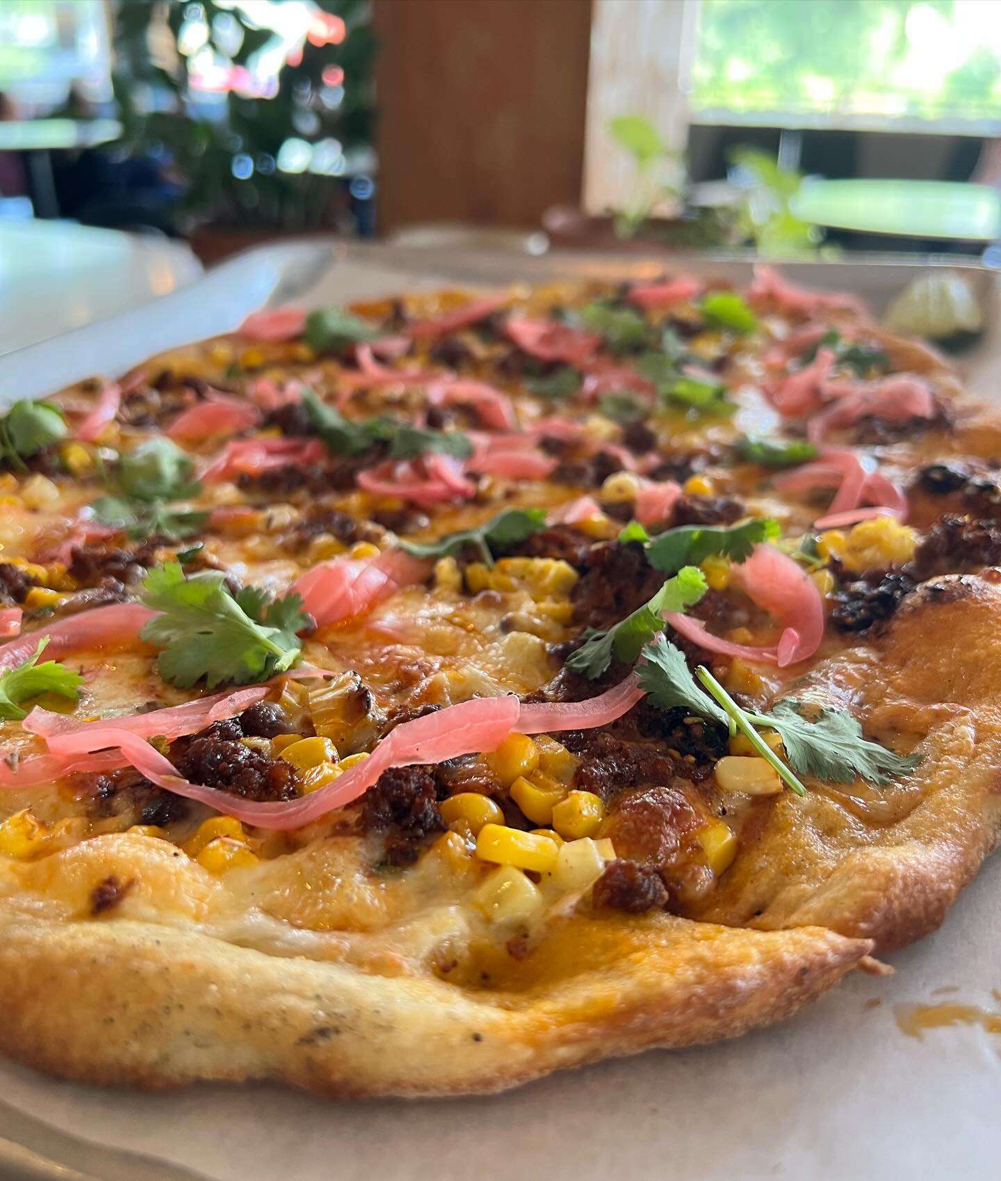 Close-up of pizza with ground meat, corn, pickled onions, and cilantro.