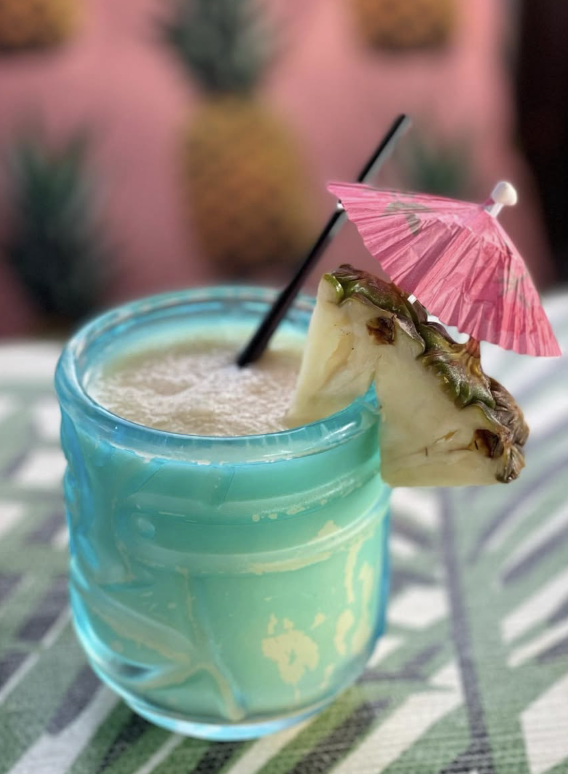 Light blue tropical drink in patterned glass with pineapple and umbrella.