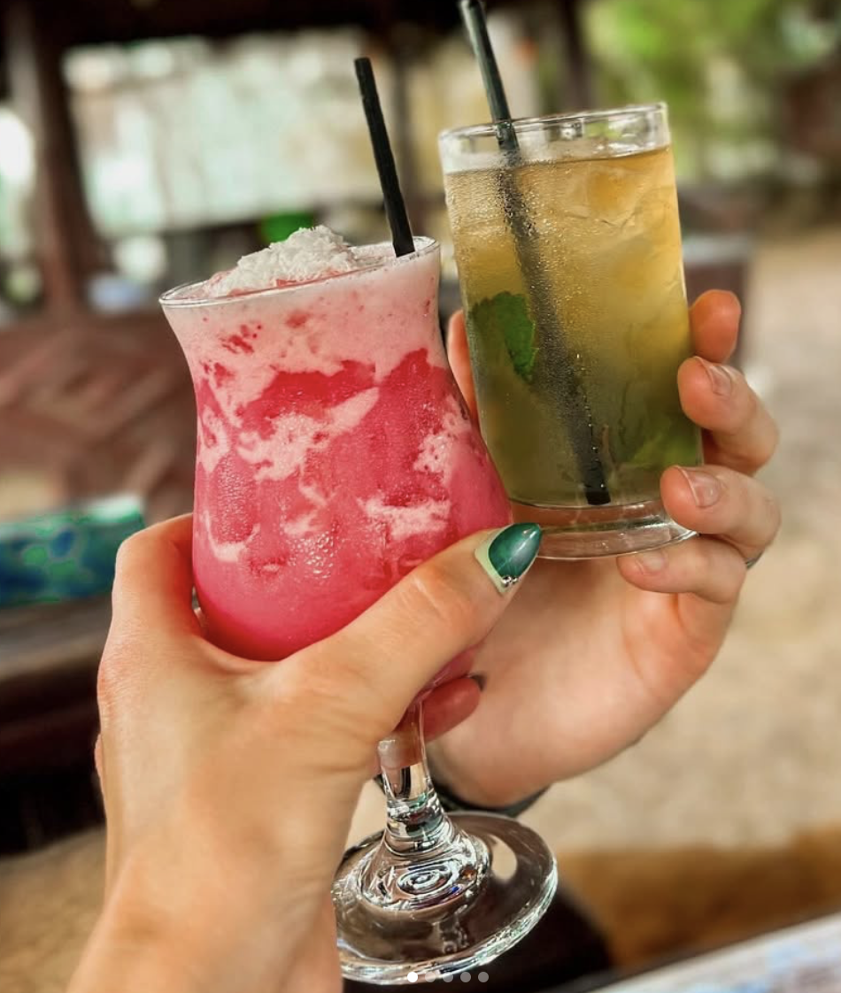 Hands holding a pink frozen drink and a green iced drink.