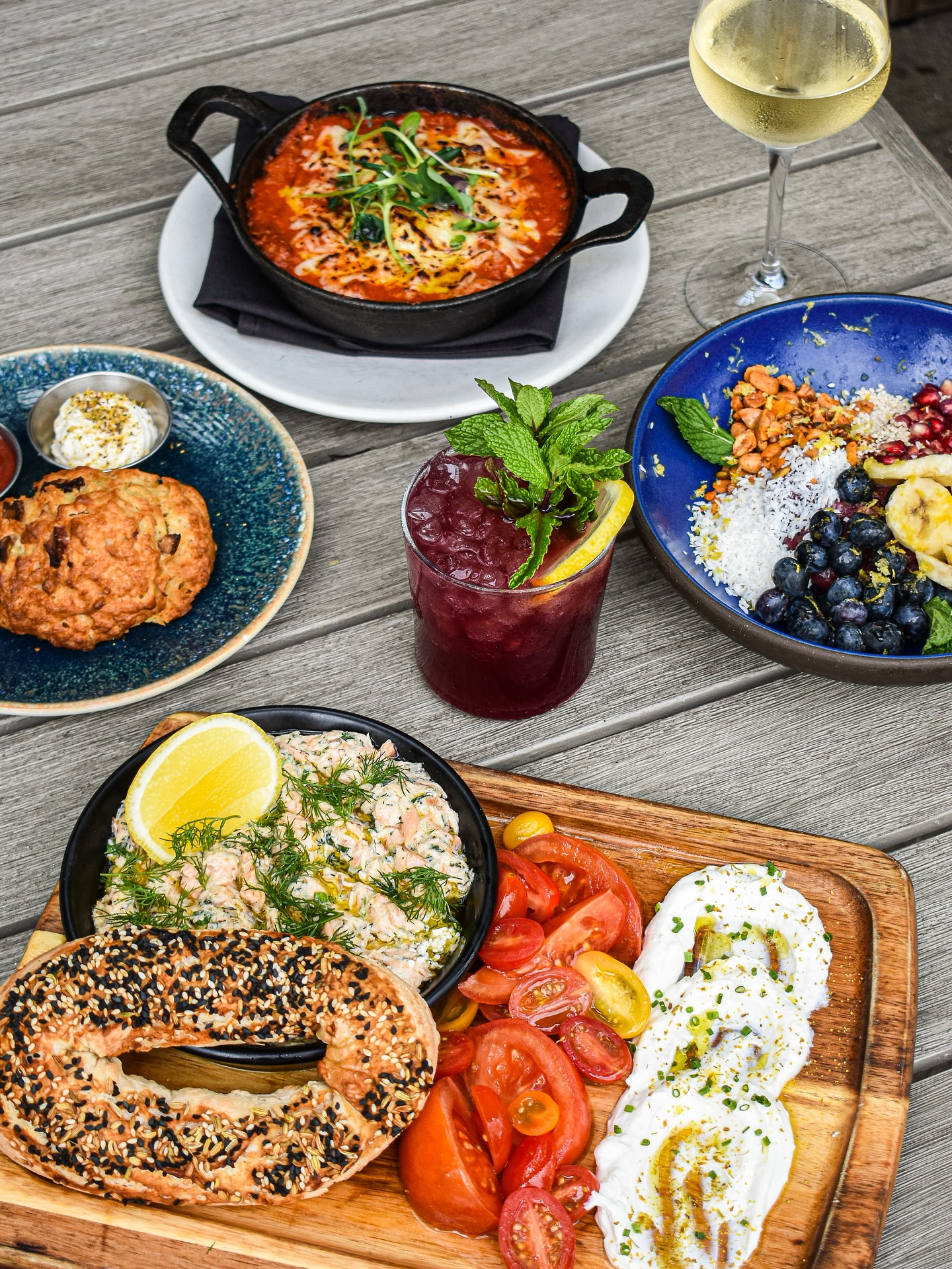 A table laden with brunch food: bagels, fruit, eggs, salmon, drinks.