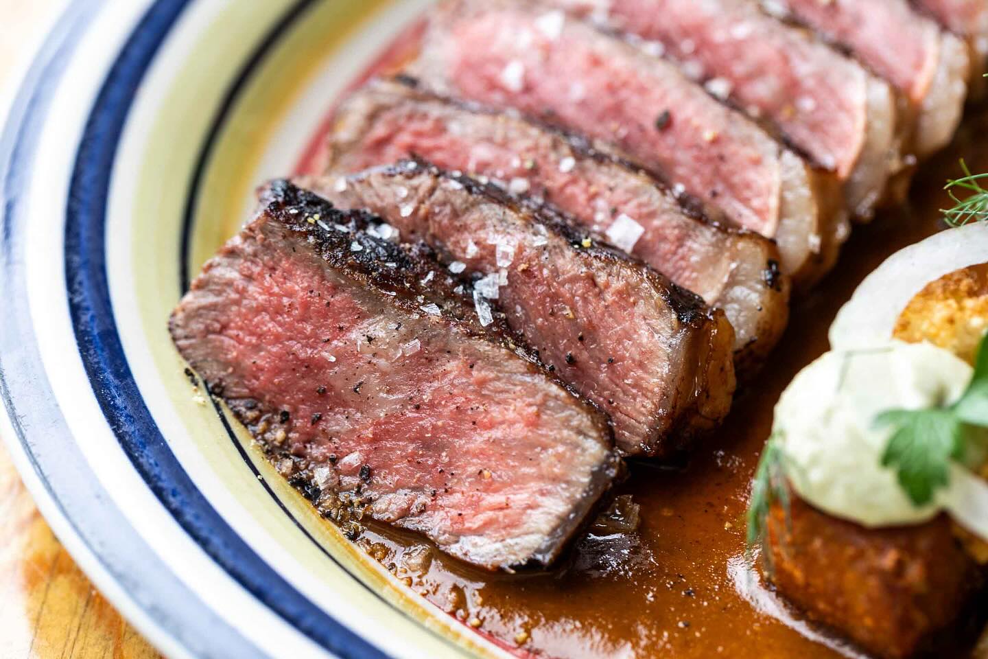 Medium-rare sliced steak seasoned with coarse salt and pepper on a plate.