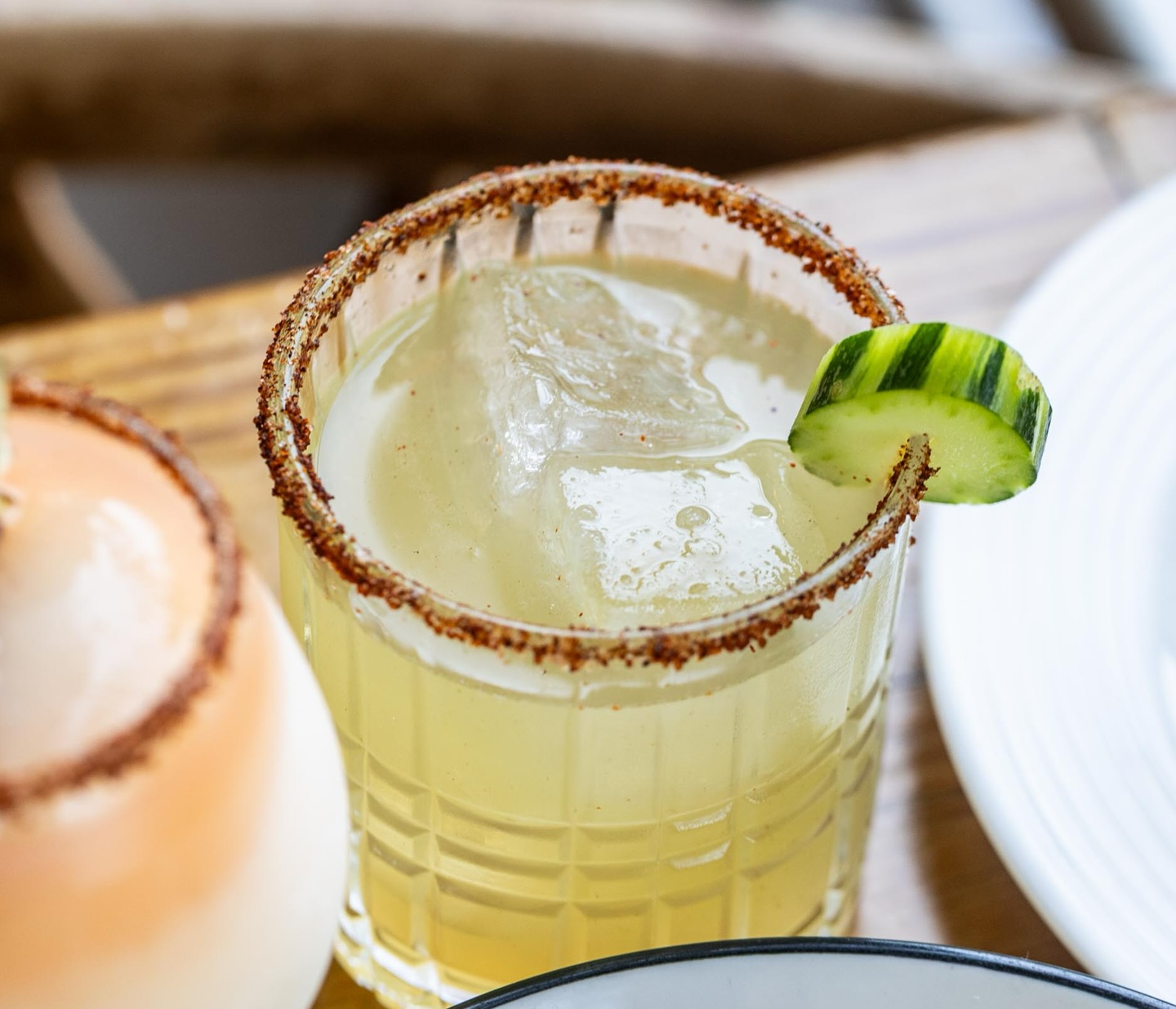 Close-up of a cocktail with ice, a spiced rim, and cucumber slice.