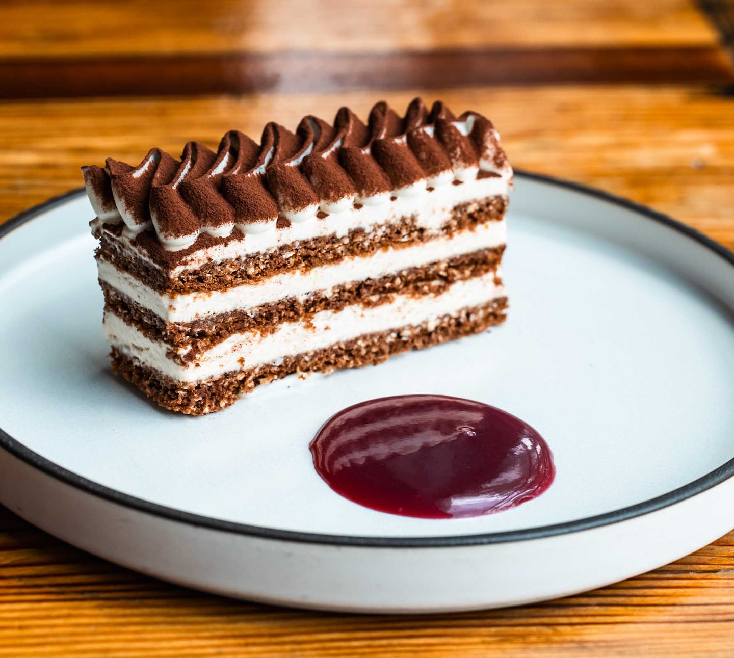 Layered chocolate and cream cake with cocoa powder, served with sauce.