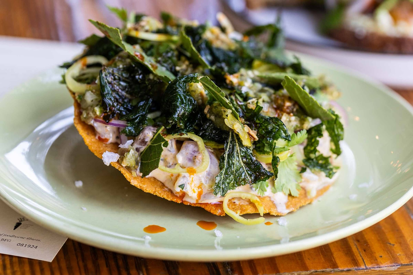 Crispy tostada with creamy filling, chili, red onion, and dark greens.