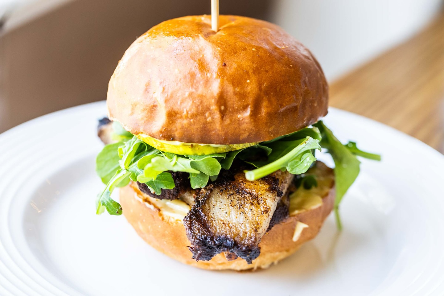Pork belly sandwich with arugula, pickle, and golden bun.