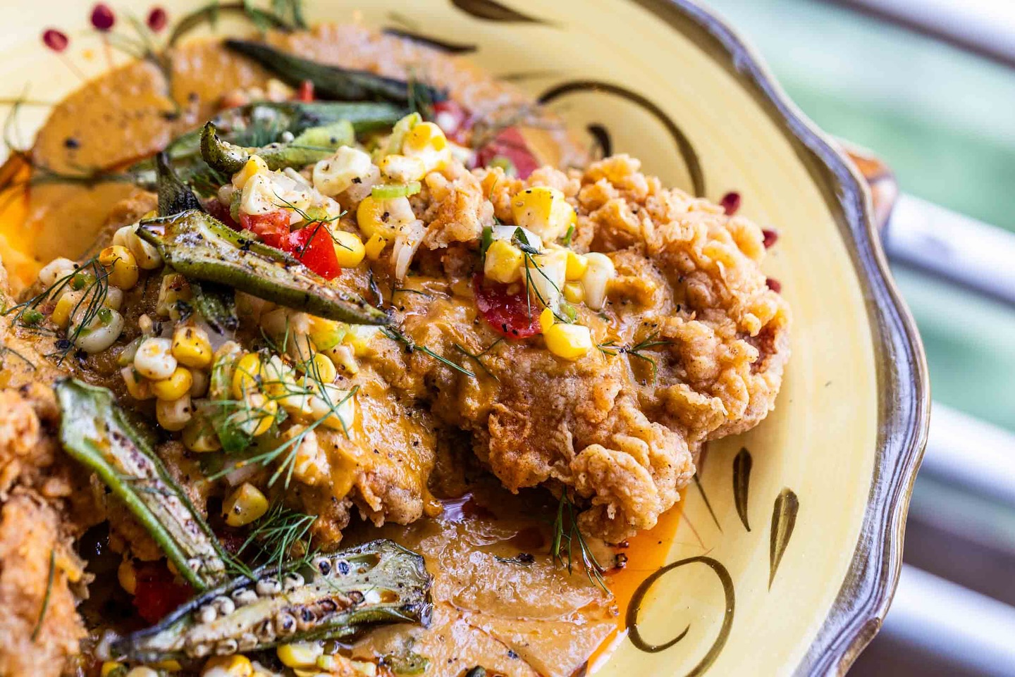 Fried chicken, okra, corn, and vegetables with sauce on a plate.