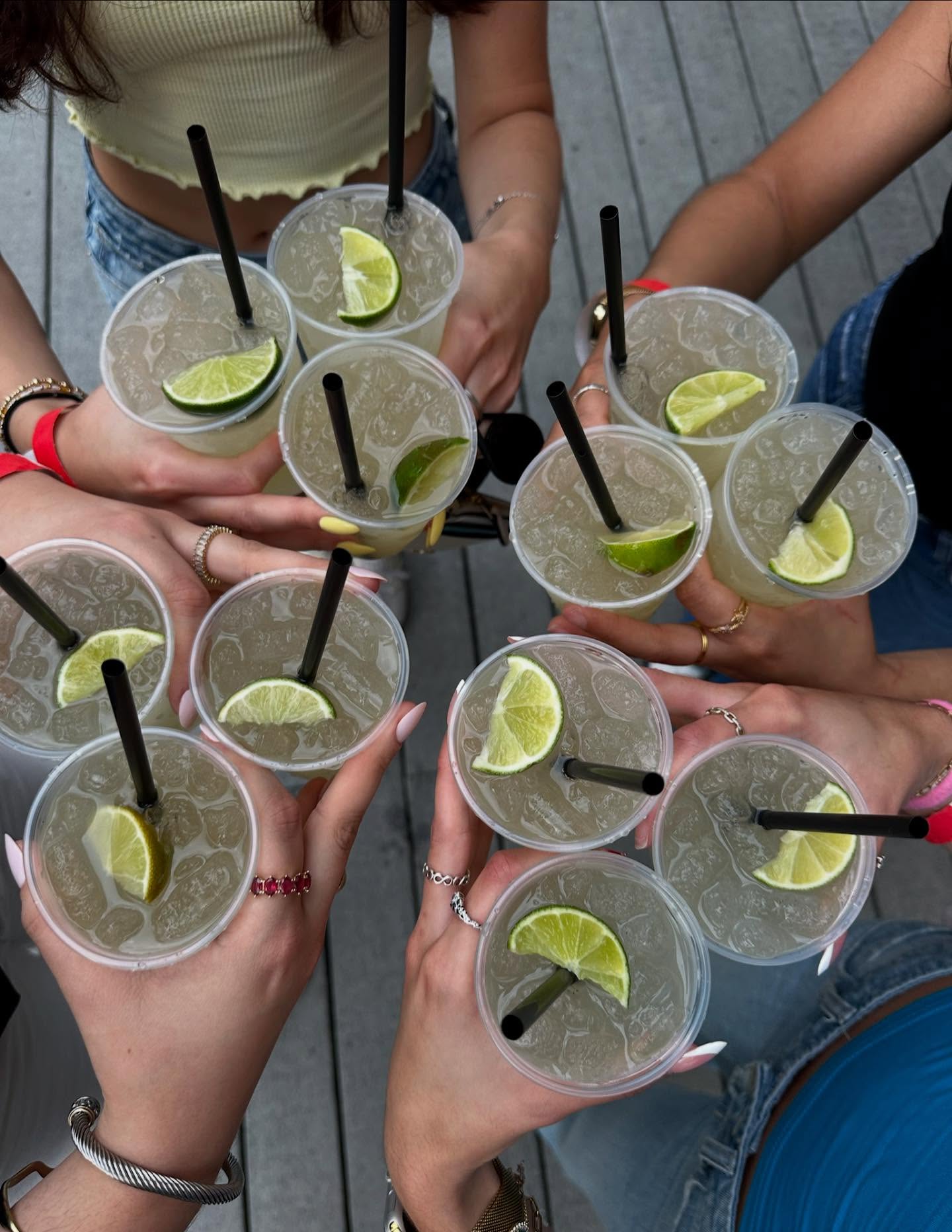Eleven cups with lime drinks and straws held by multiple hands.