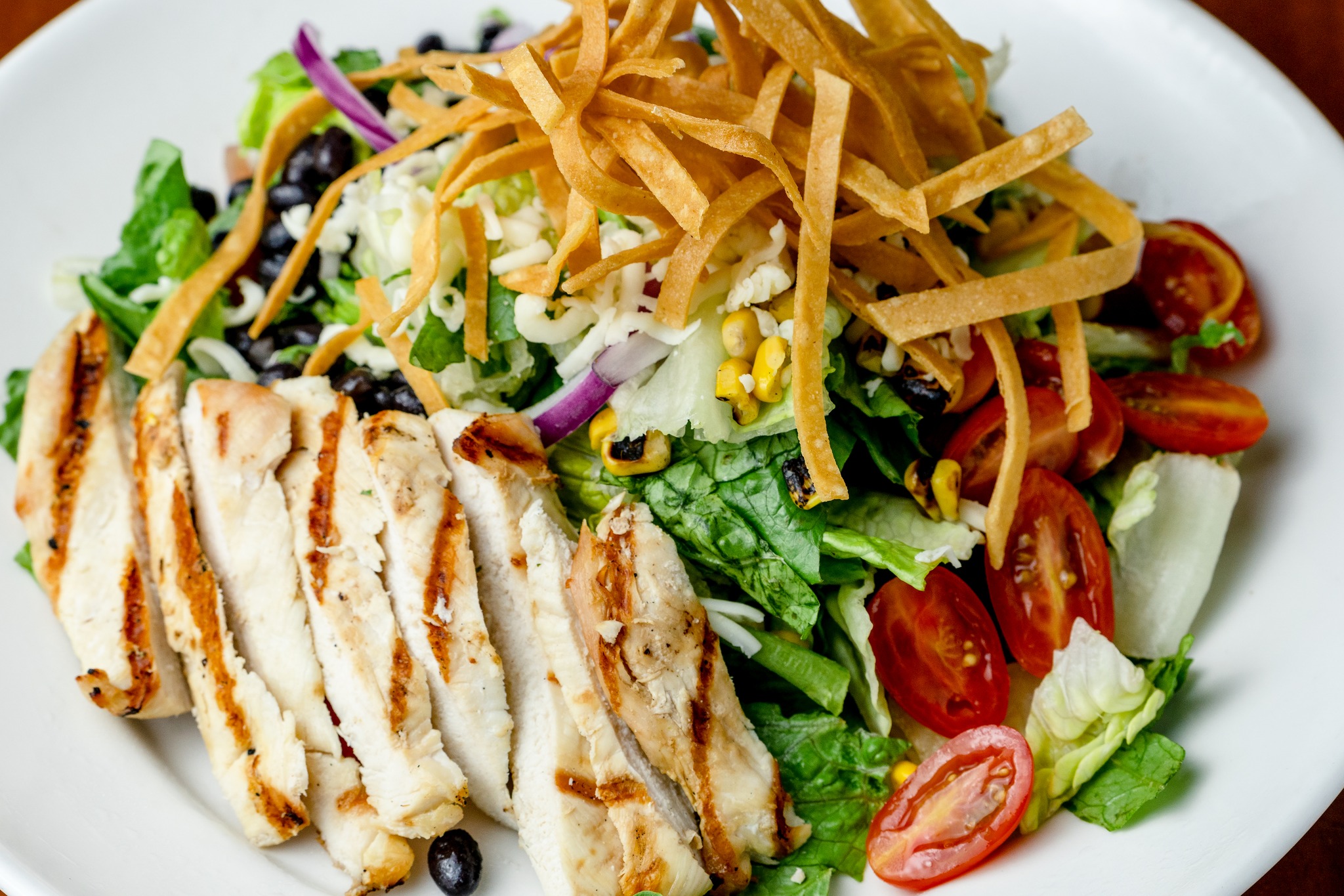 Grilled chicken salad with vegetables, cheese, and tortilla strips.