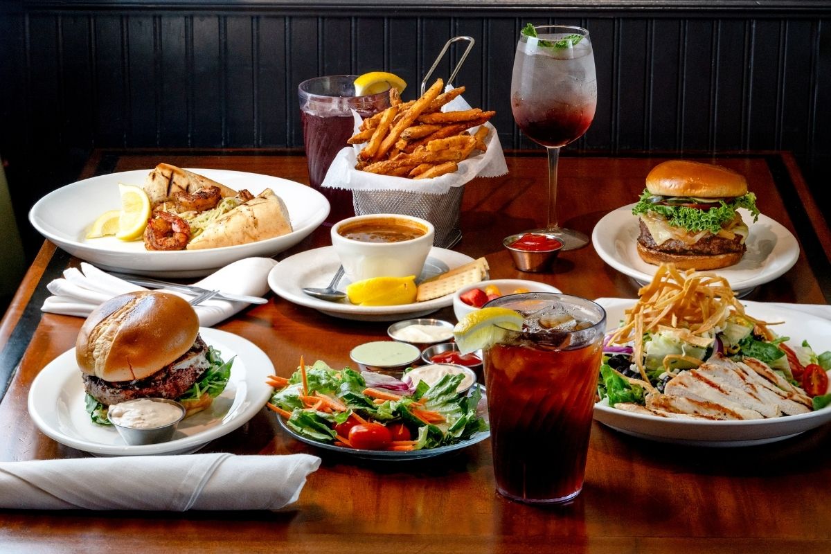 Table with two burgers, two salads, shrimp, fries, soup, and drinks.