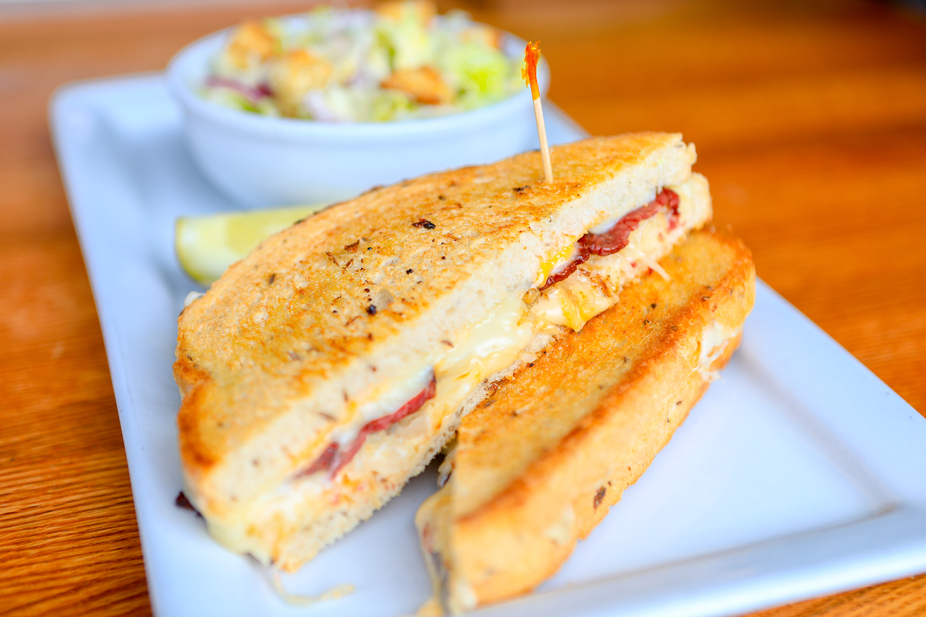 Grilled sandwich with melted cheese and meat, lemon, side salad.