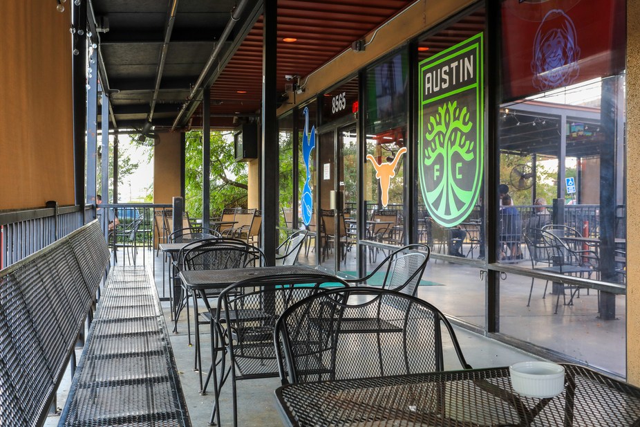 Restaurant patio with black mesh tables, chairs, and Austin FC logo.