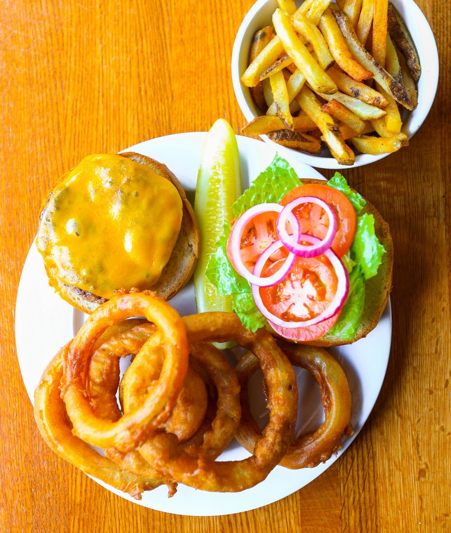 Cheeseburger, onion rings, french fries, and pickle on a wooden table.