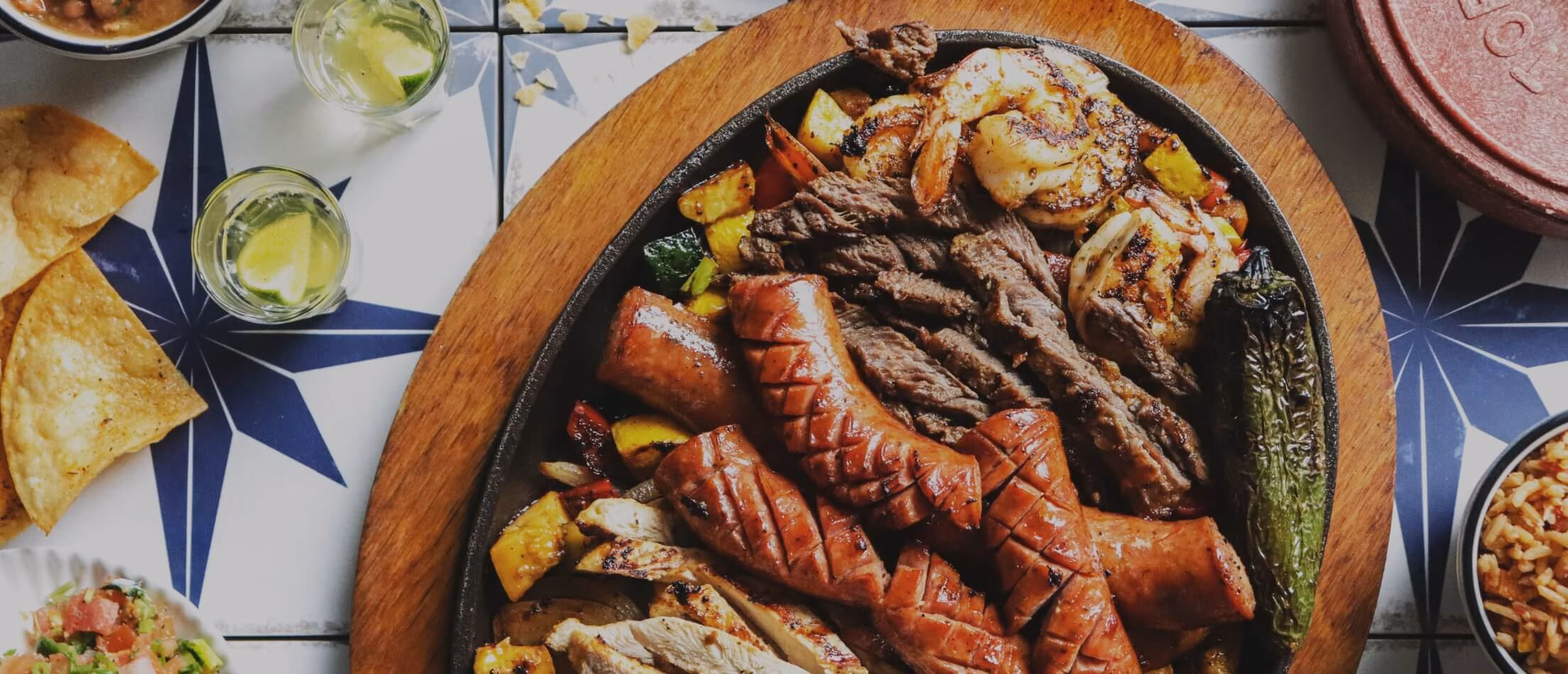 Large grilled platter with shrimp, steak, sausages, chicken, and vegetables.