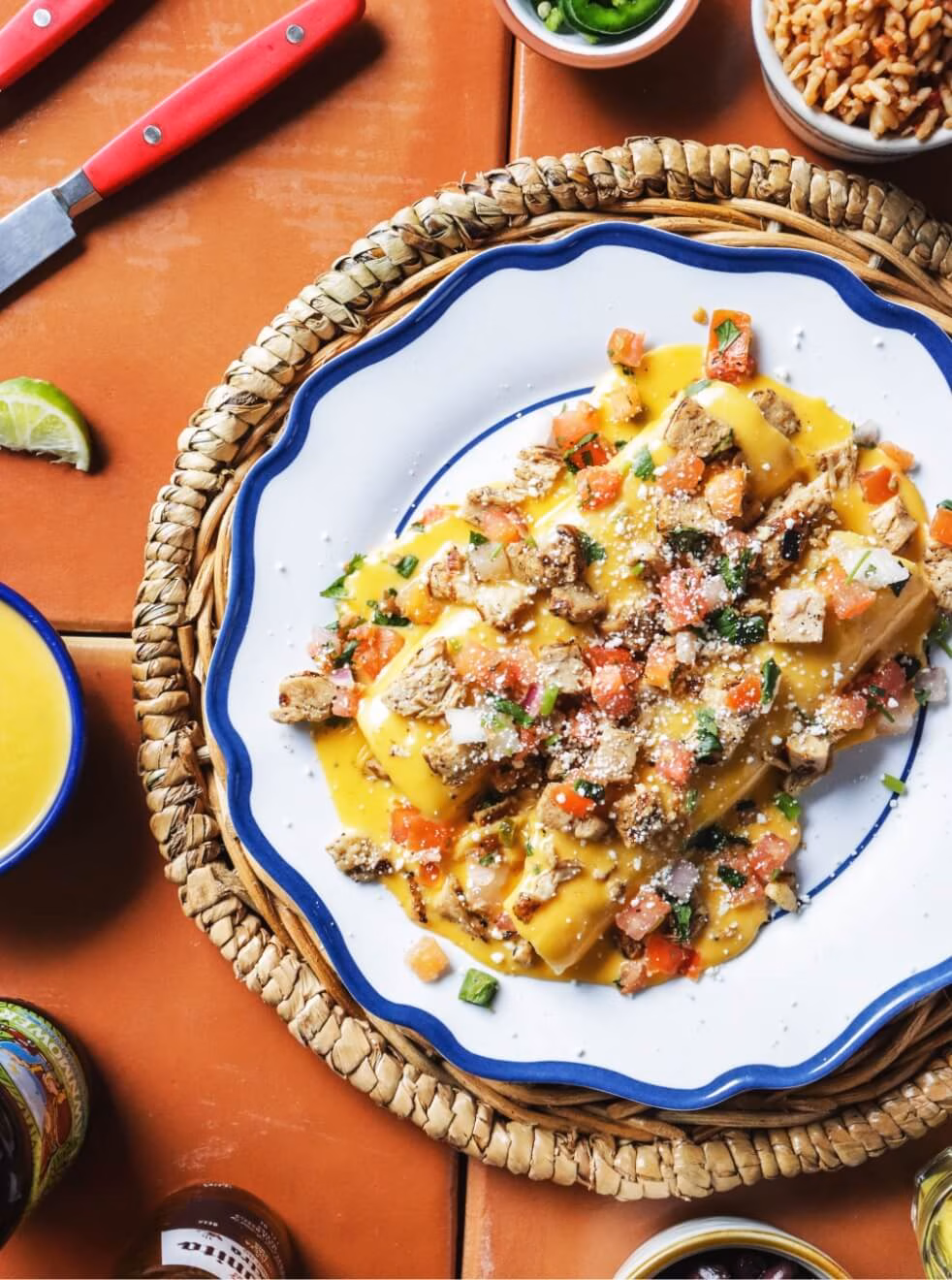 Rolled items covered in cheese sauce, topped with meat, tomatoes, and cheese.