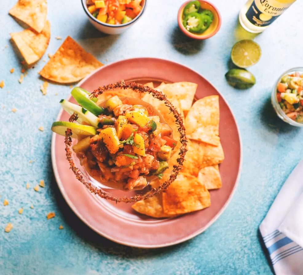 Ceviche in a glass with tortilla chips, limes, and beer.