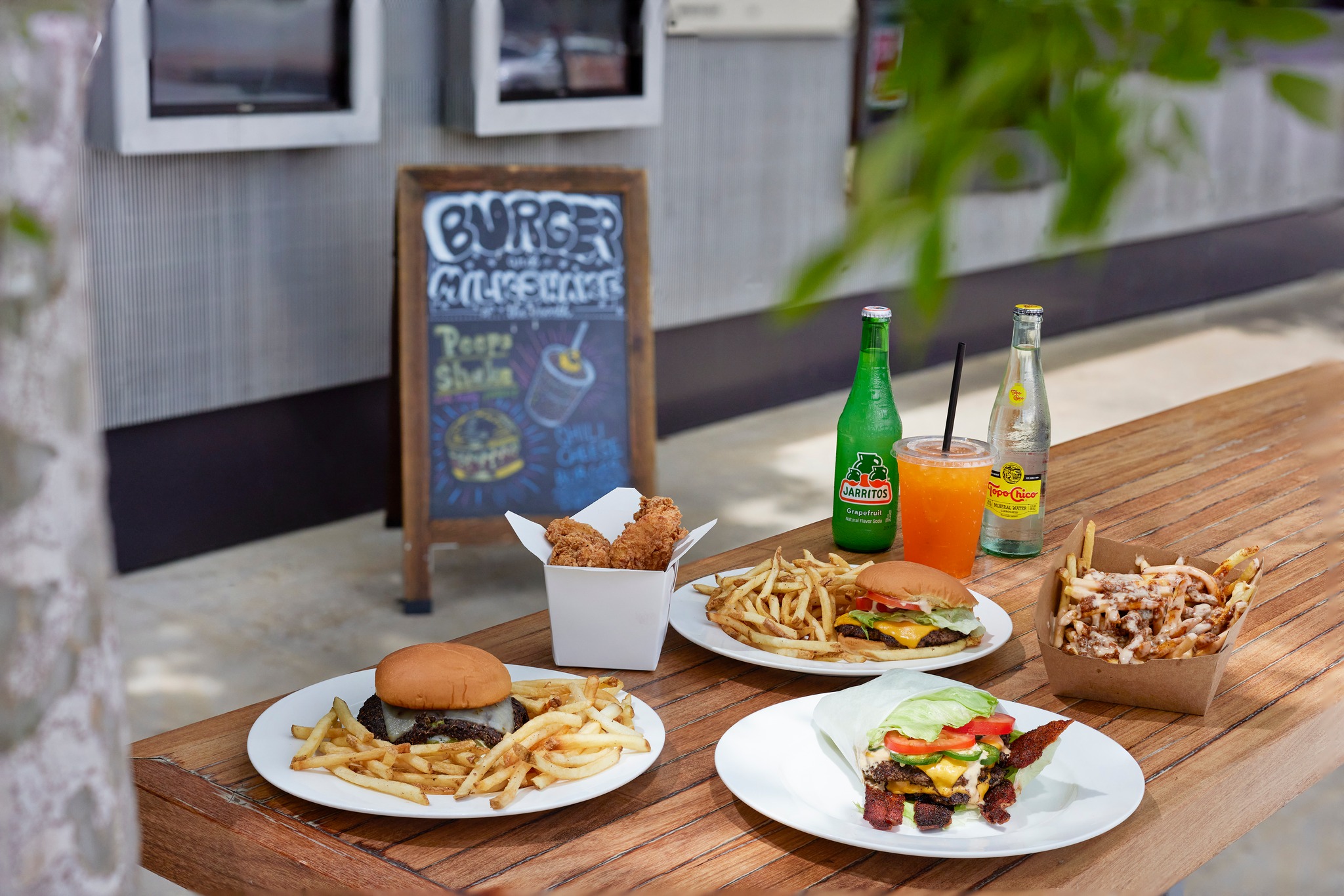 Outdoor table with burgers, fries, chicken tenders, and drinks.