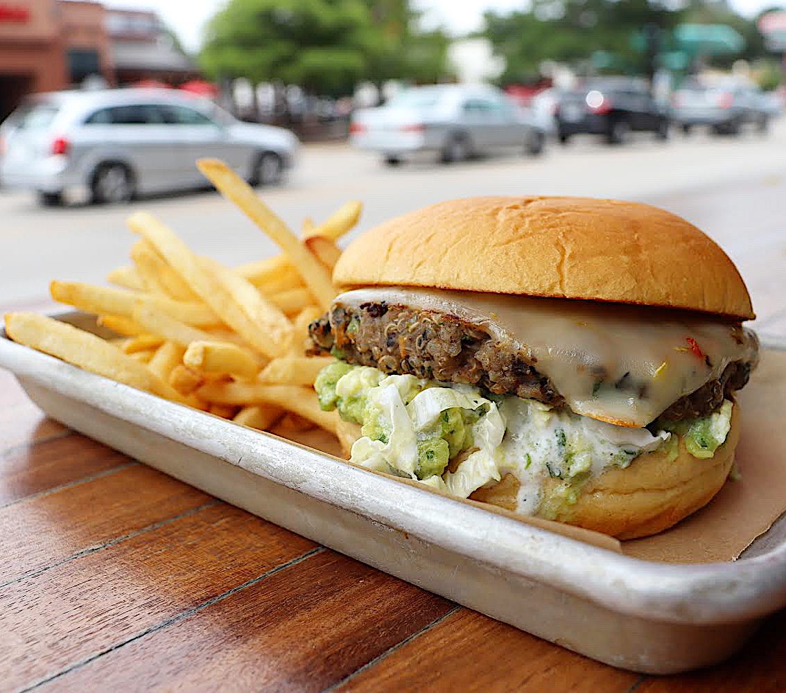 Veggie burger with melted cheese and fries on a tray outdoors.