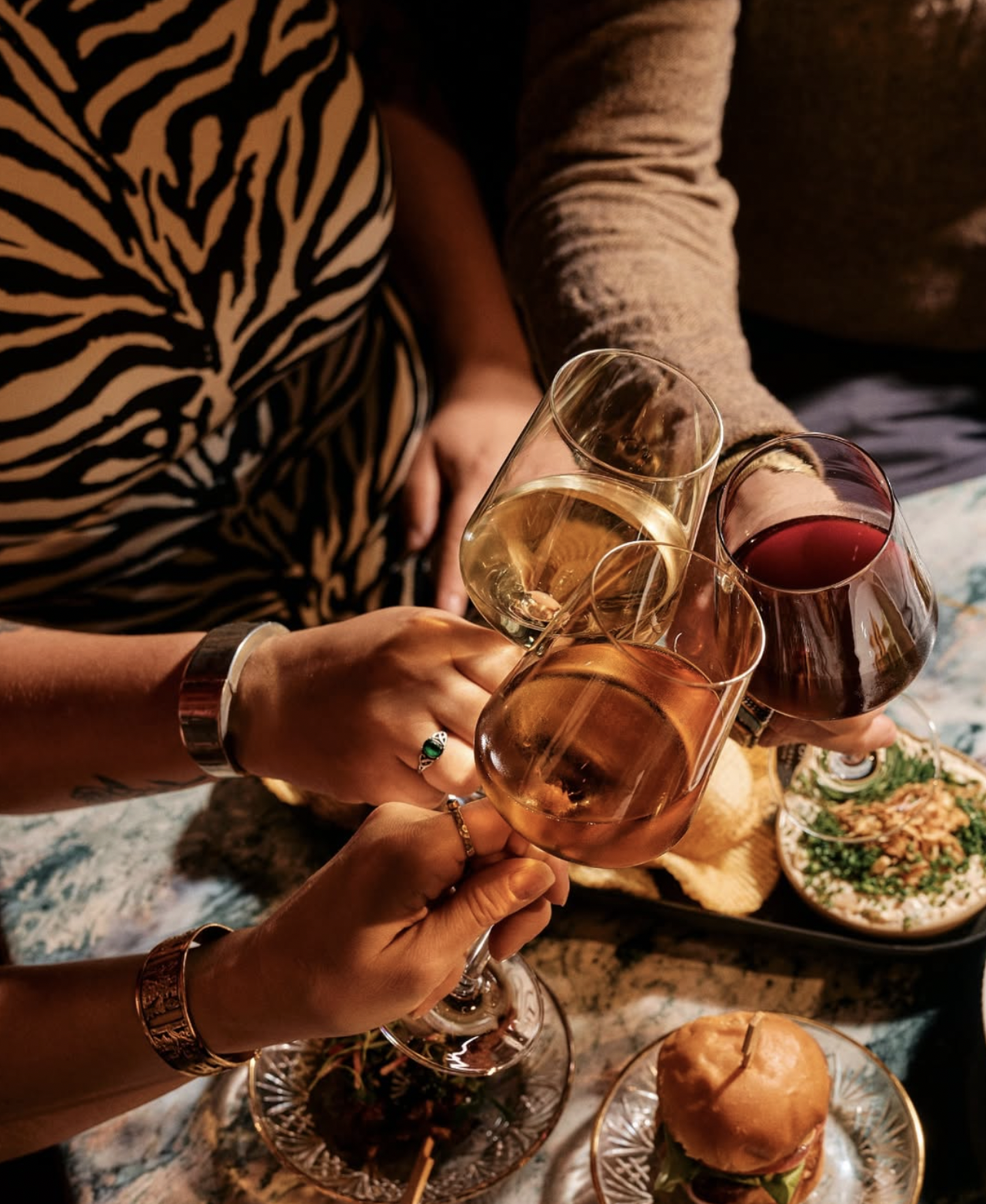 Hands clinking glasses of white, rosé, and red wine, with food.