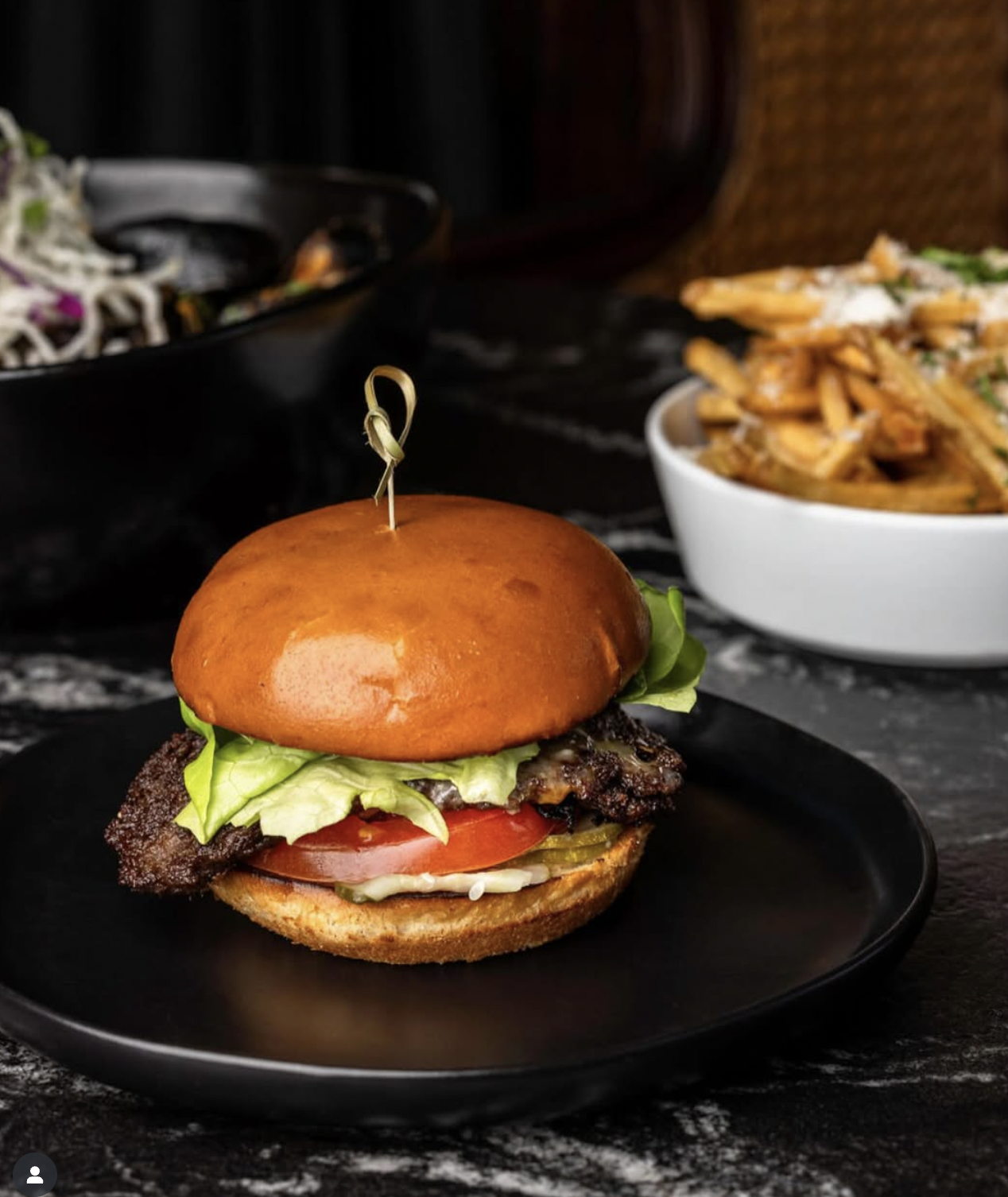 Burger, fries, and side salad on a black plate, marble surface.