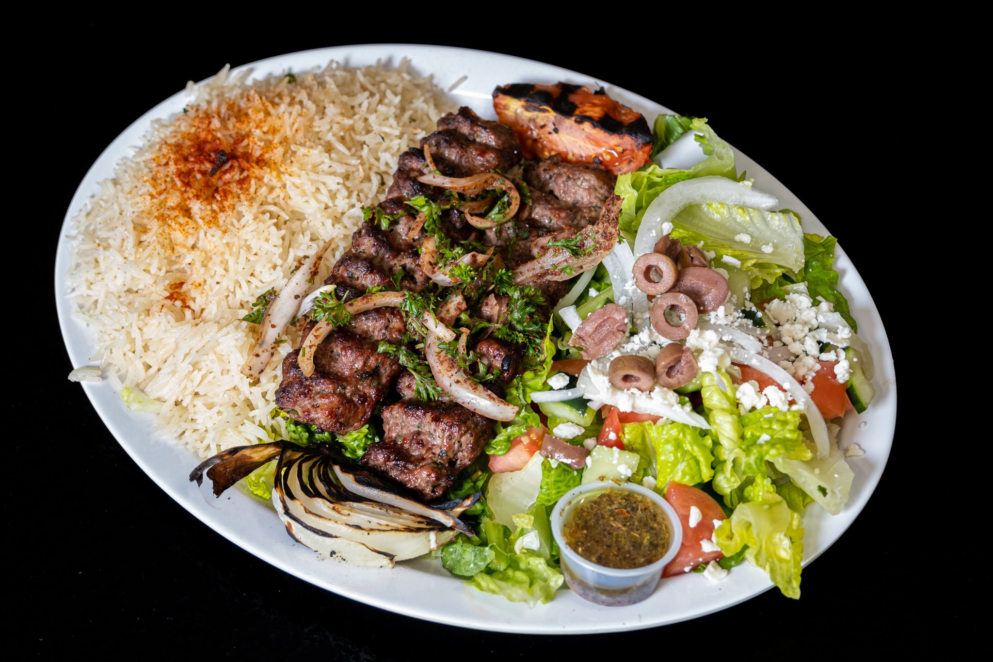 Platter with grilled meat, rice, fresh salad, grilled vegetables, and dipping sauce.