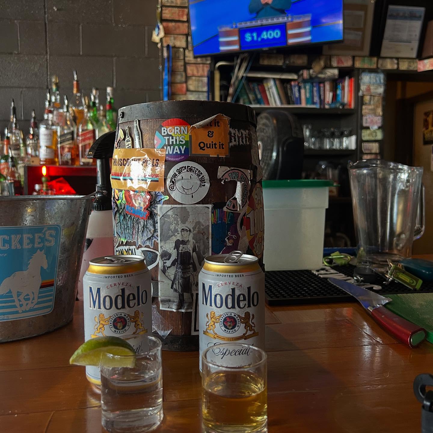 A bar scene with beer cans, shots, and a TV playing Jeopardy.
