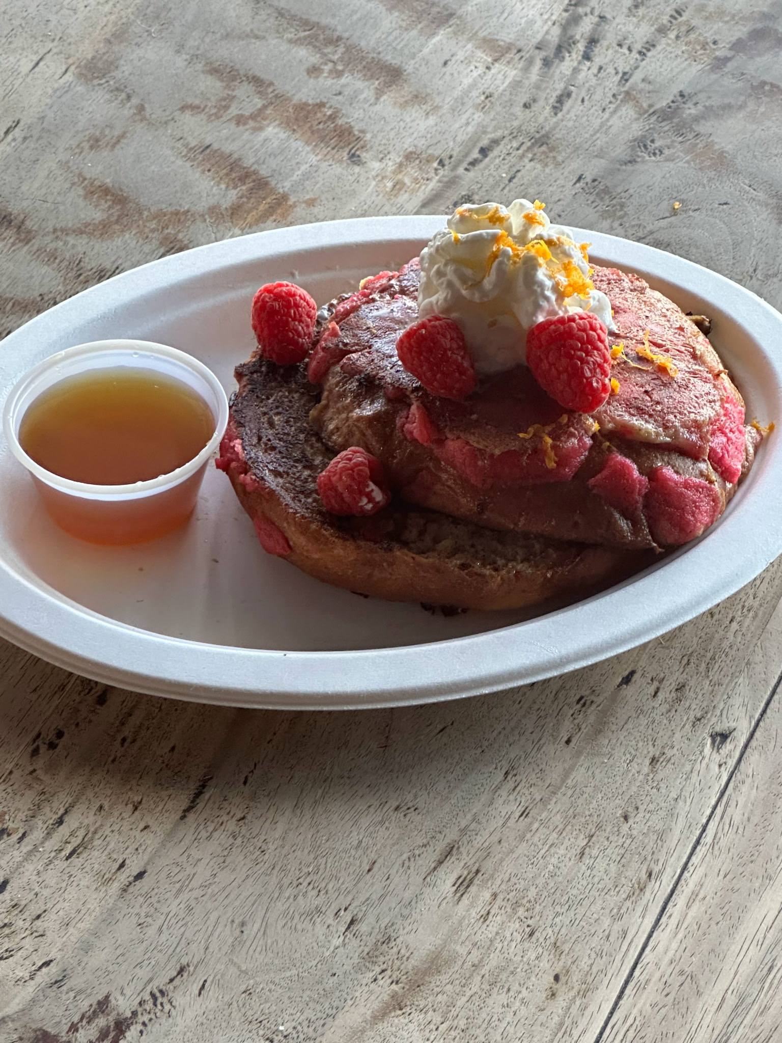 Red pancakes with raspberries, whipped cream, orange zest, and syrup.